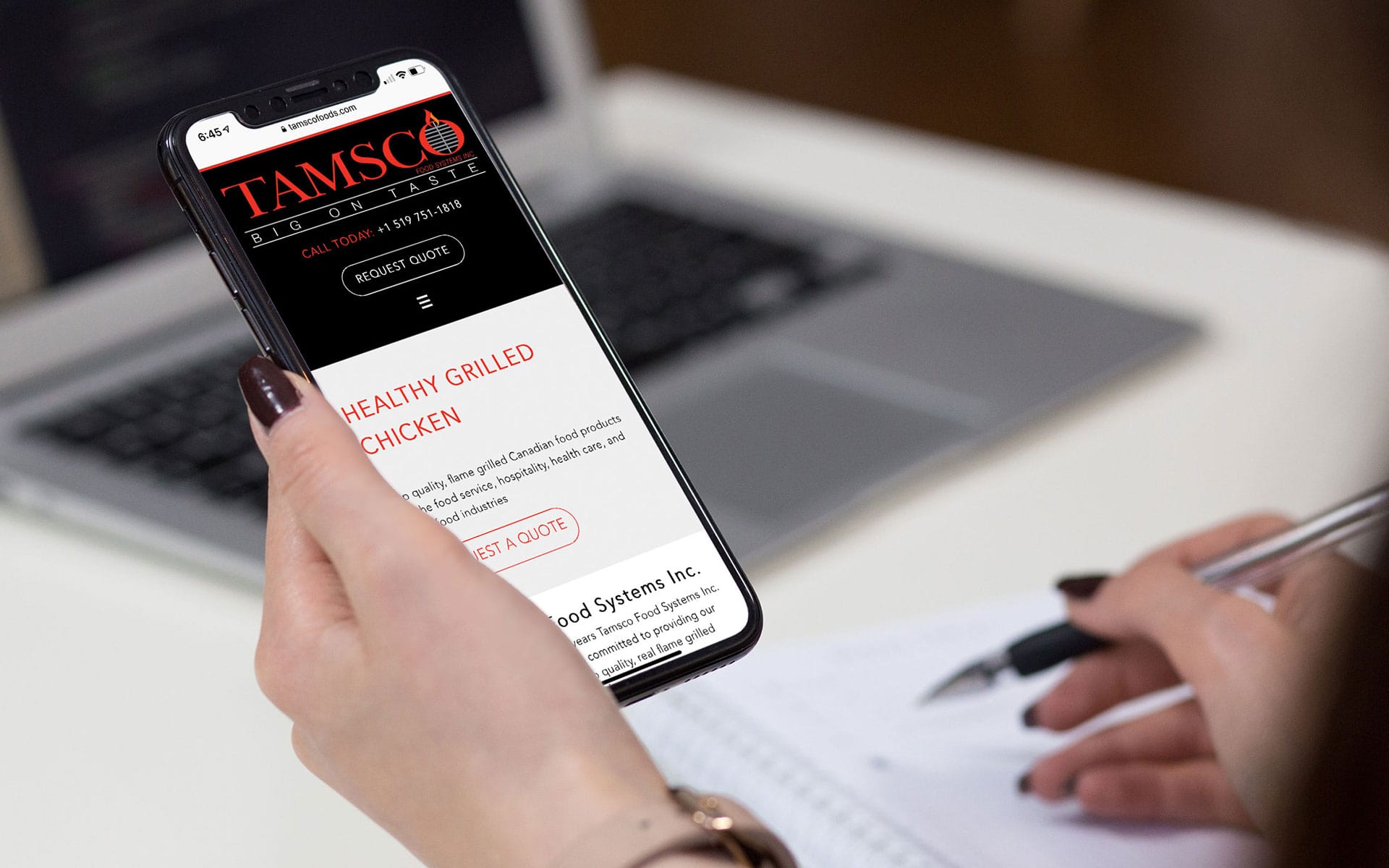 Tamsco Food Systems home page displayed on an iPhone being held by a woman.