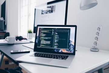 Laptop computer on white desk displaying computer code.